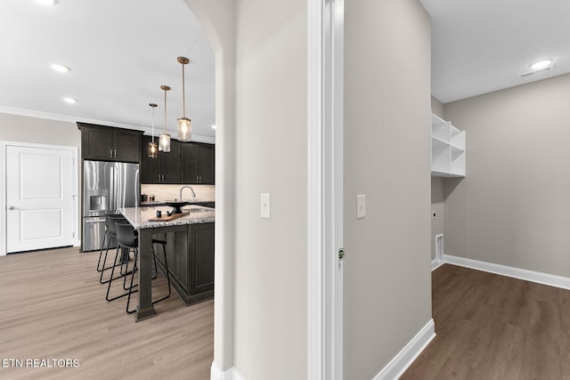 kitchen featuring light wood-type flooring, stainless steel refrigerator with ice dispenser, a kitchen bar, and light stone countertops