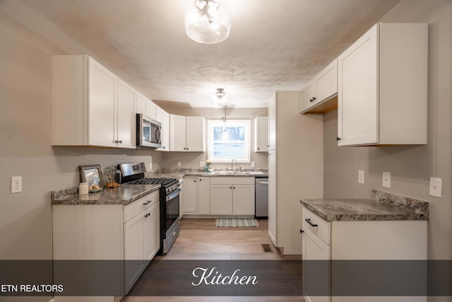 kitchen with appliances with stainless steel finishes, stone countertops, white cabinetry, sink, and dark wood-type flooring