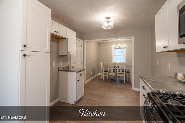 kitchen with dark wood-type flooring, a chandelier, dark stone countertops, appliances with stainless steel finishes, and white cabinets