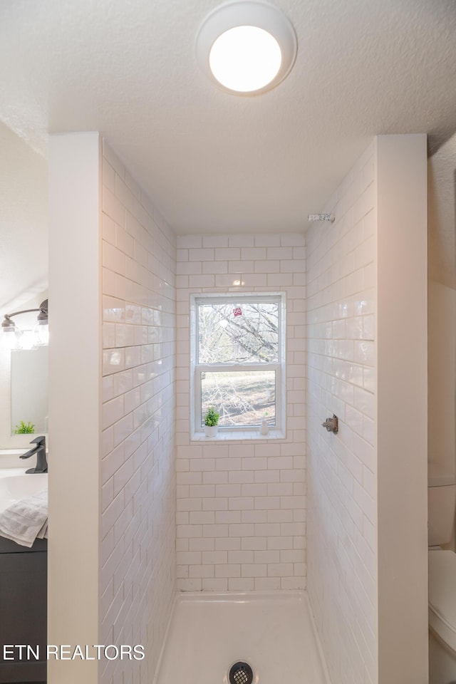 bathroom featuring a tile shower, vanity, toilet, and a textured ceiling