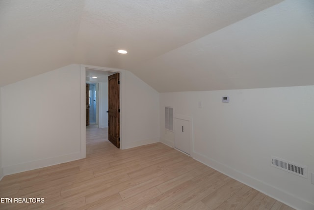 additional living space with lofted ceiling, a textured ceiling, and light wood-type flooring