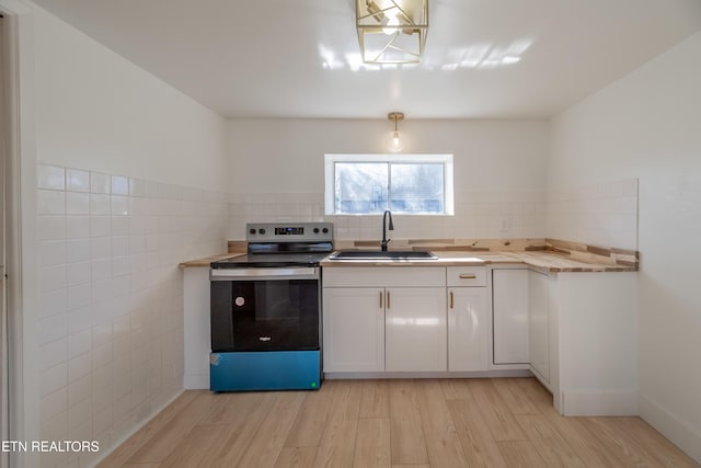 kitchen with sink, stainless steel electric range, wooden counters, and white cabinets