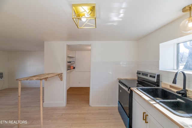 kitchen featuring sink, white cabinetry, pendant lighting, stainless steel electric stove, and light hardwood / wood-style floors