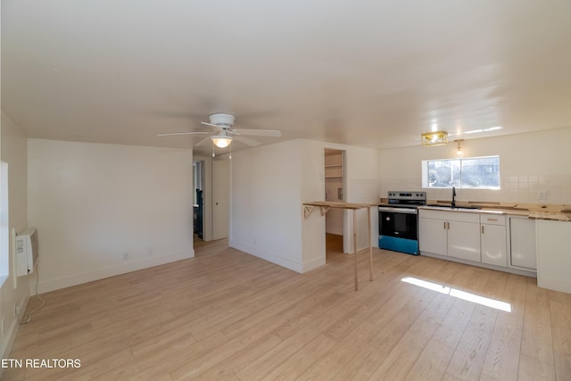 kitchen with stainless steel electric stove, sink, white cabinets, decorative backsplash, and light hardwood / wood-style floors