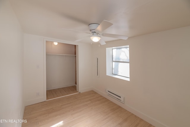 unfurnished bedroom featuring ceiling fan, a baseboard radiator, a closet, and light wood-type flooring