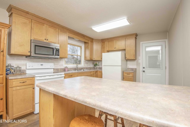 kitchen featuring light brown cabinetry, sink, a breakfast bar area, light wood-type flooring, and white appliances