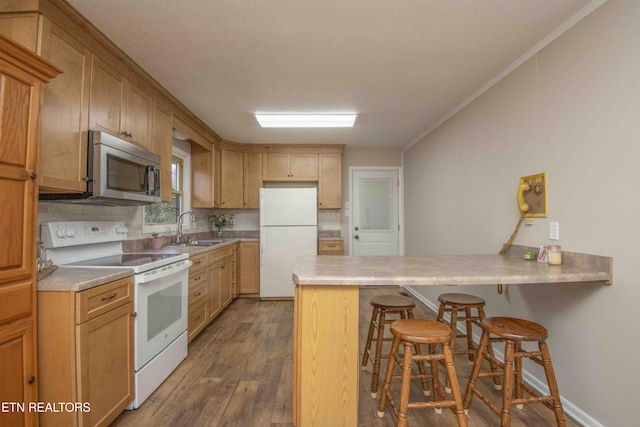 kitchen featuring sink, dark hardwood / wood-style floors, a kitchen breakfast bar, kitchen peninsula, and white appliances