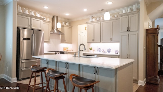 kitchen with a kitchen island with sink, pendant lighting, stainless steel refrigerator, and wall chimney exhaust hood