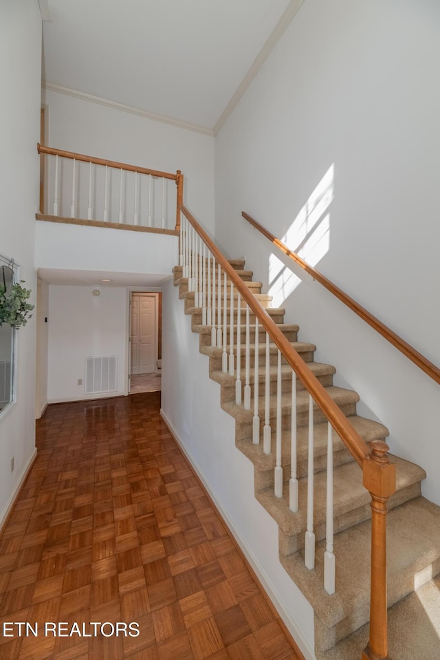 staircase featuring a high ceiling, crown molding, and parquet floors