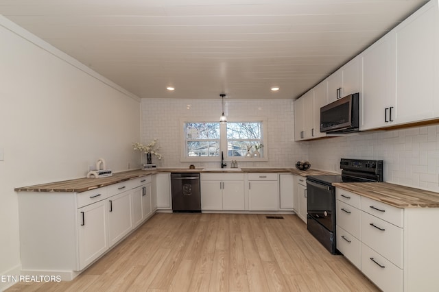 kitchen with butcher block counters, backsplash, white cabinets, black appliances, and light wood-type flooring