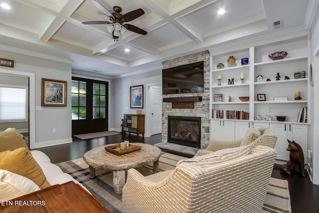 living room with crown molding, dark wood-type flooring, coffered ceiling, a stone fireplace, and beamed ceiling