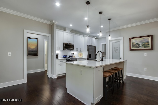 kitchen with hanging light fixtures, white cabinetry, appliances with stainless steel finishes, and an island with sink