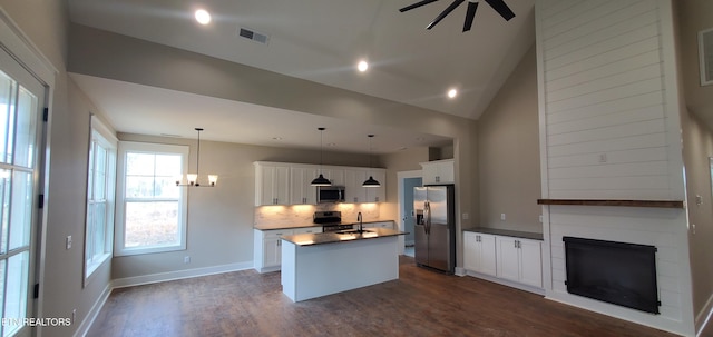 kitchen with dark wood-type flooring, appliances with stainless steel finishes, a kitchen island with sink, white cabinets, and decorative light fixtures