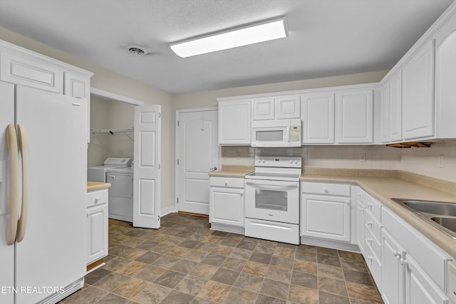 kitchen with white appliances, washer and dryer, and white cabinets