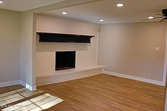 unfurnished living room with a brick fireplace, hardwood / wood-style floors, and ceiling fan