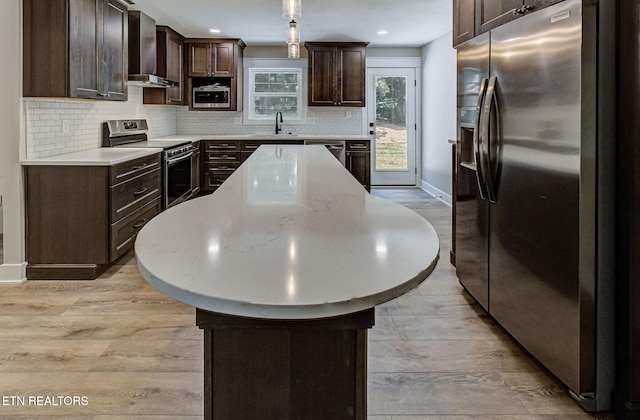 kitchen featuring a sink, light countertops, appliances with stainless steel finishes, wall chimney range hood, and a center island