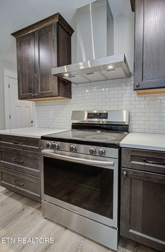 kitchen featuring wall chimney range hood, stainless steel electric range oven, light countertops, and light wood finished floors