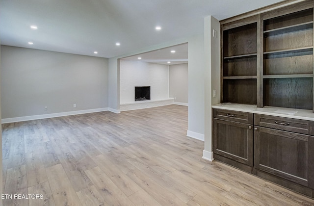 unfurnished living room featuring a large fireplace, built in features, and light hardwood / wood-style floors