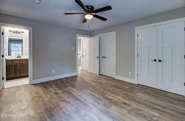 unfurnished bedroom featuring baseboards, ensuite bath, light wood-style flooring, multiple closets, and a sink