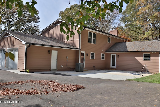 exterior space featuring central AC unit, a chimney, roof with shingles, an attached garage, and board and batten siding