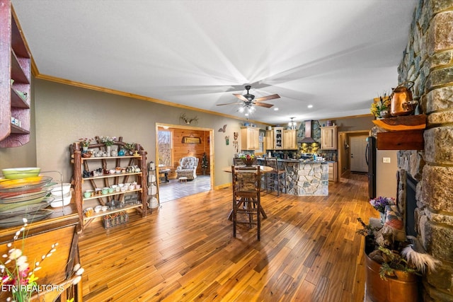 living room with crown molding, light hardwood / wood-style flooring, a stone fireplace, and ceiling fan