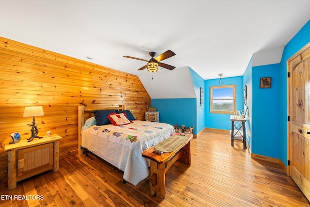 bedroom featuring ceiling fan, lofted ceiling, wood-type flooring, and wood walls