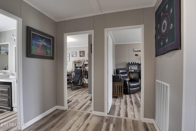 hallway with ornamental molding and light hardwood / wood-style floors