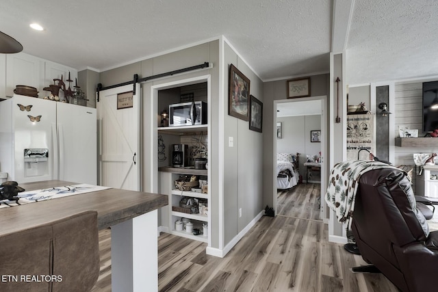 kitchen featuring crown molding, hardwood / wood-style floors, white fridge with ice dispenser, a textured ceiling, and a barn door