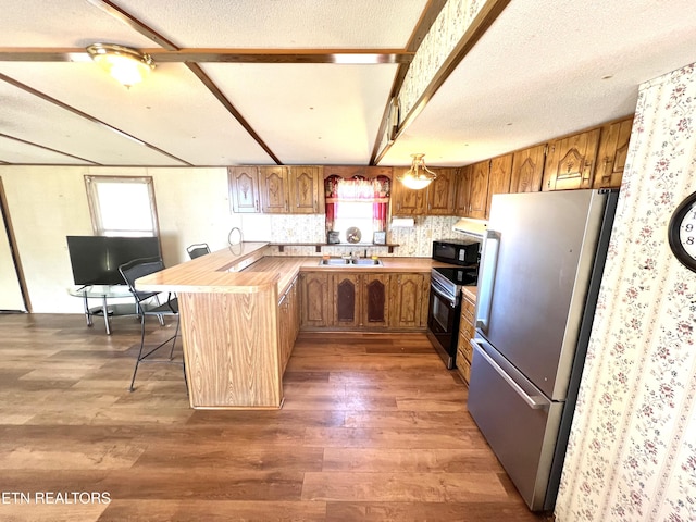 kitchen with range with electric cooktop, sink, stainless steel fridge, a kitchen breakfast bar, and kitchen peninsula