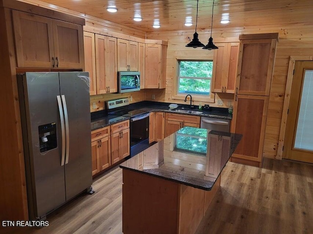 kitchen featuring appliances with stainless steel finishes, pendant lighting, sink, dark stone counters, and light hardwood / wood-style floors