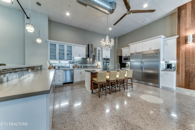 kitchen with pendant lighting, wall chimney range hood, white cabinetry, a towering ceiling, and built in appliances