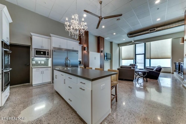 kitchen featuring sink, tasteful backsplash, built in appliances, a kitchen island with sink, and white cabinets