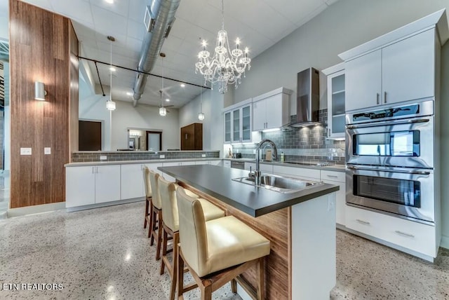 kitchen with white cabinetry, stainless steel double oven, wall chimney exhaust hood, and sink