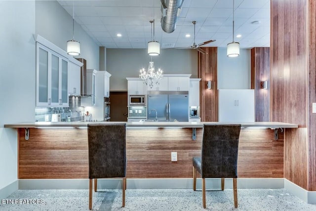 kitchen featuring built in appliances, white cabinets, and decorative light fixtures