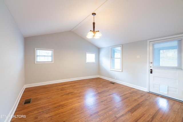 spare room with hardwood / wood-style flooring, lofted ceiling, and an inviting chandelier