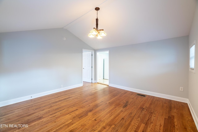 unfurnished room featuring lofted ceiling, hardwood / wood-style floors, and a notable chandelier