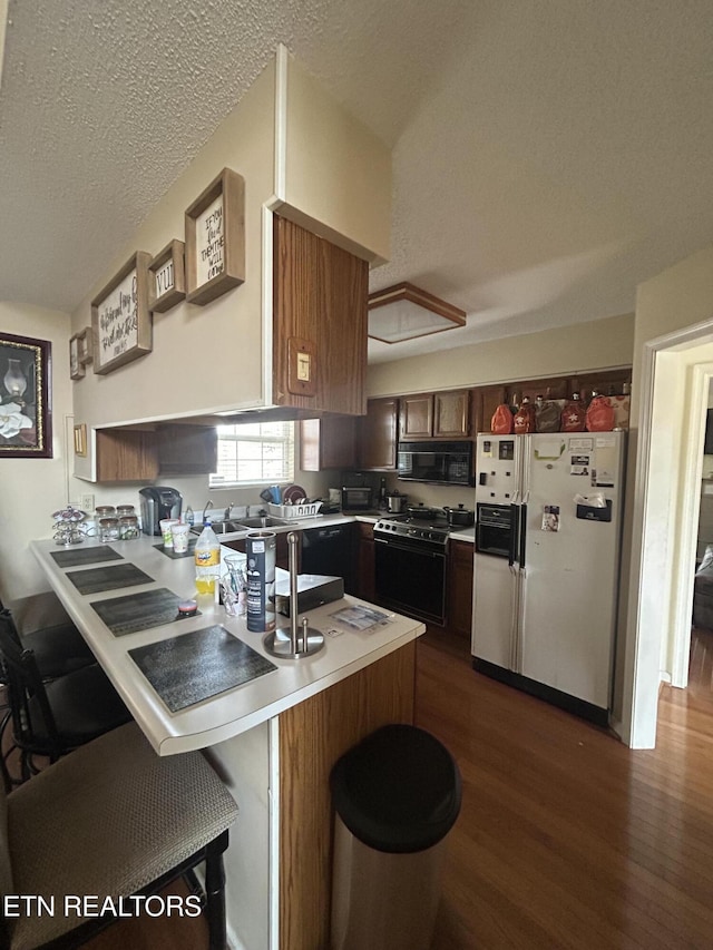 kitchen with a breakfast bar area, dark hardwood / wood-style floors, black appliances, a textured ceiling, and kitchen peninsula