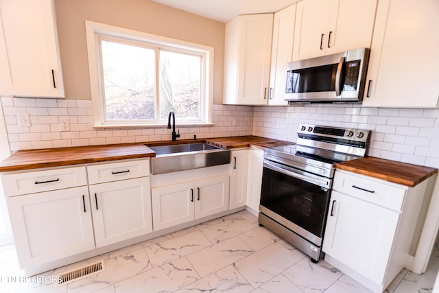 kitchen with butcher block counters, sink, white cabinetry, stainless steel appliances, and backsplash