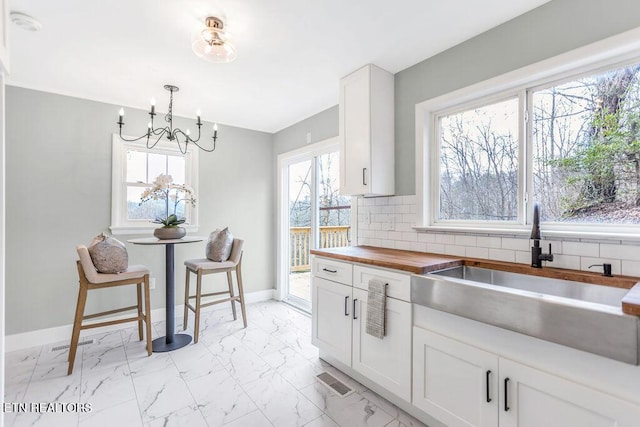 kitchen featuring pendant lighting, sink, butcher block countertops, white cabinetry, and decorative backsplash