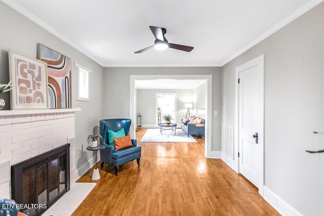 living area with crown molding, a brick fireplace, ceiling fan, and light wood-type flooring