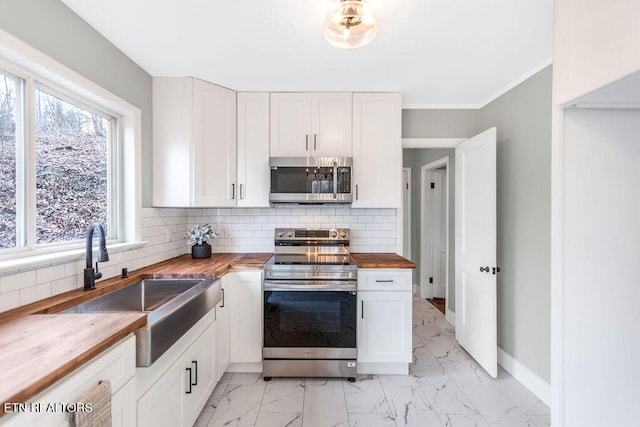 kitchen featuring sink, wooden counters, appliances with stainless steel finishes, backsplash, and white cabinets