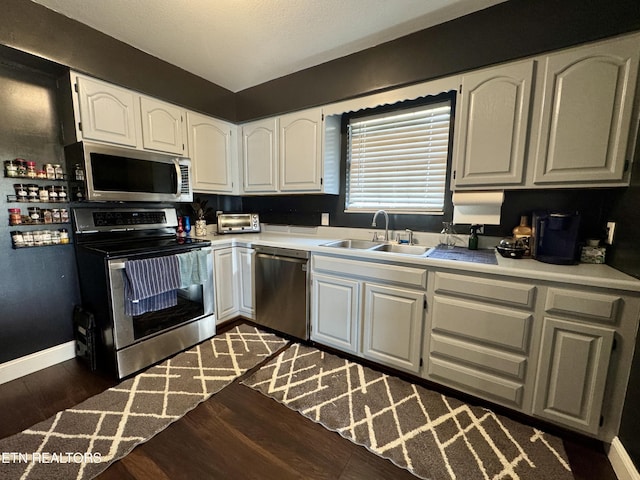 kitchen with appliances with stainless steel finishes, sink, white cabinets, and dark hardwood / wood-style flooring