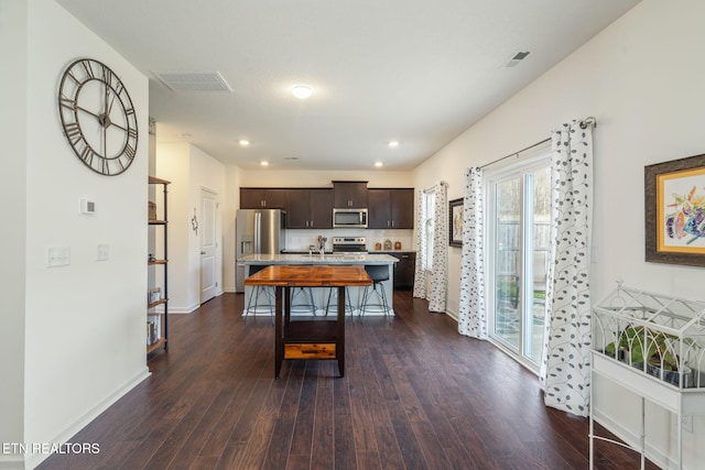 kitchen featuring a breakfast bar area, dark brown cabinets, a center island with sink, appliances with stainless steel finishes, and dark hardwood / wood-style flooring