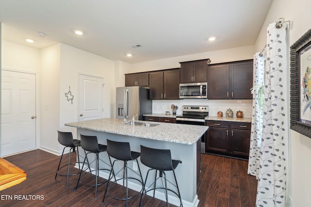 kitchen with a breakfast bar, dark hardwood / wood-style flooring, dark brown cabinetry, stainless steel appliances, and a center island with sink