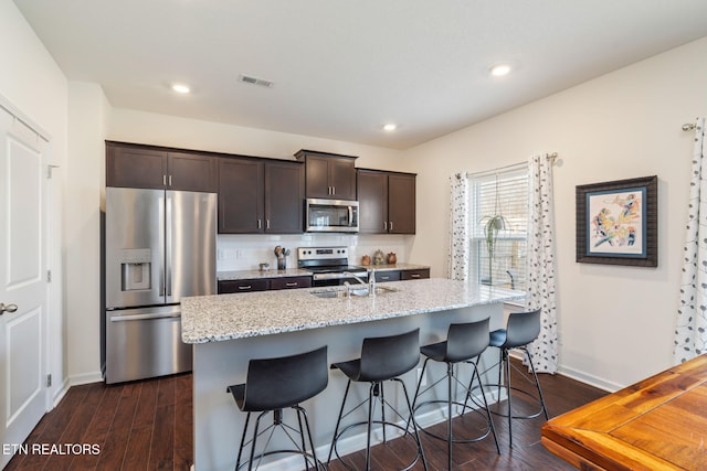 kitchen with appliances with stainless steel finishes, dark hardwood / wood-style floors, a center island with sink, and dark brown cabinetry