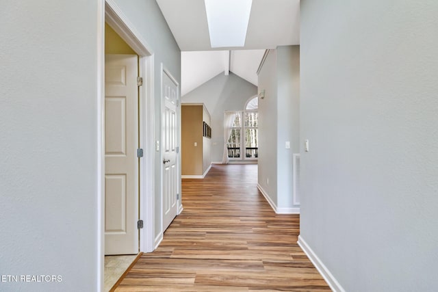 corridor with visible vents, vaulted ceiling with skylight, light wood-style floors, and baseboards