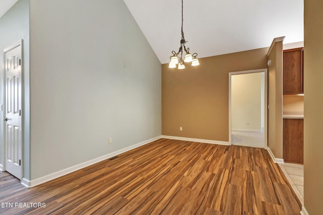 unfurnished dining area featuring baseboards, an inviting chandelier, wood finished floors, and vaulted ceiling