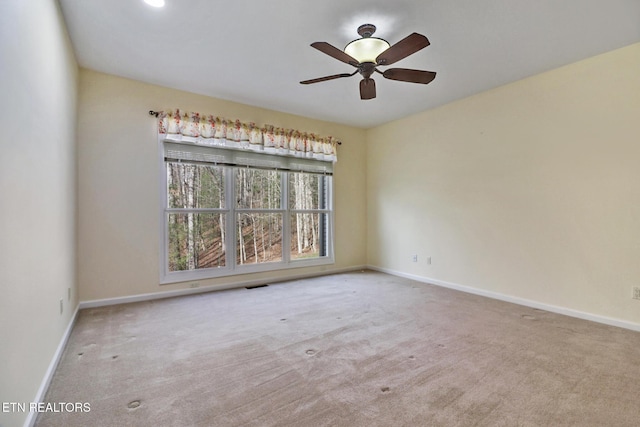 carpeted spare room with visible vents, a ceiling fan, and baseboards