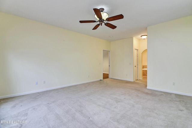 carpeted spare room featuring baseboards, arched walkways, and a ceiling fan