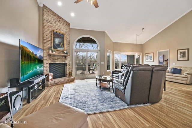 living room featuring high vaulted ceiling, a fireplace, ornamental molding, ceiling fan, and light wood-type flooring